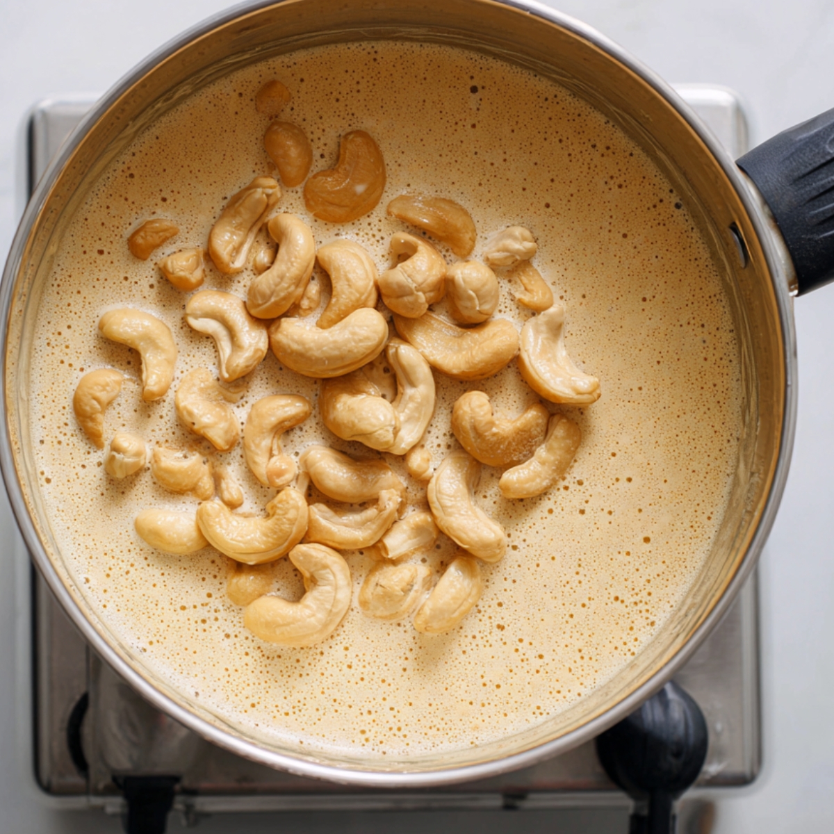 A close-up shot of a pan filled with cashew nuts floating on top of a creamy liquid mixture.