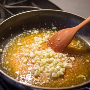 Chopped garlic sautéing in melted butter in a frying pan, with the wooden spoon stirring the mixture.
