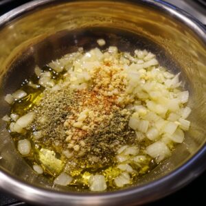 Chopped onions sautéing in olive oil with garlic, herbs, and spices in a stainless steel pan.