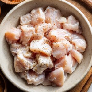 Bowl of raw chicken pieces seasoned with salt, pepper, and spices, ready for cooking.