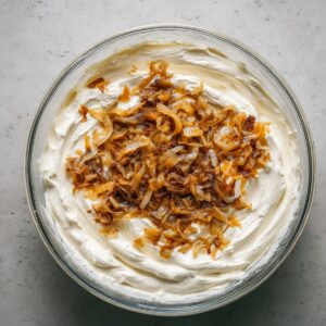 A bowl of creamy dip topped with golden caramelized onions, surrounded by a smooth white dip base.