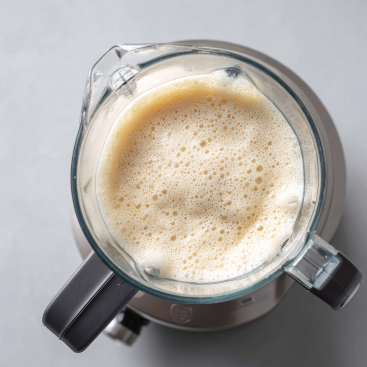 “Blender filled with frothy piña colada mixture, showing a creamy and smooth texture from above.”
