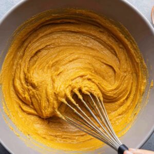 Bowl of pumpkin pie filling mixture with a whisk, featuring a thick orange batter consistency.
