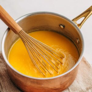 A saucepan filled with smooth pumpkin spice syrup being whisked, showing a rich orange color and creamy texture.