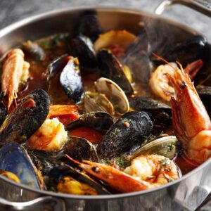 Pan of seafood stew featuring mussels, shrimp, clams, and prawns simmering in a rich tomato broth.