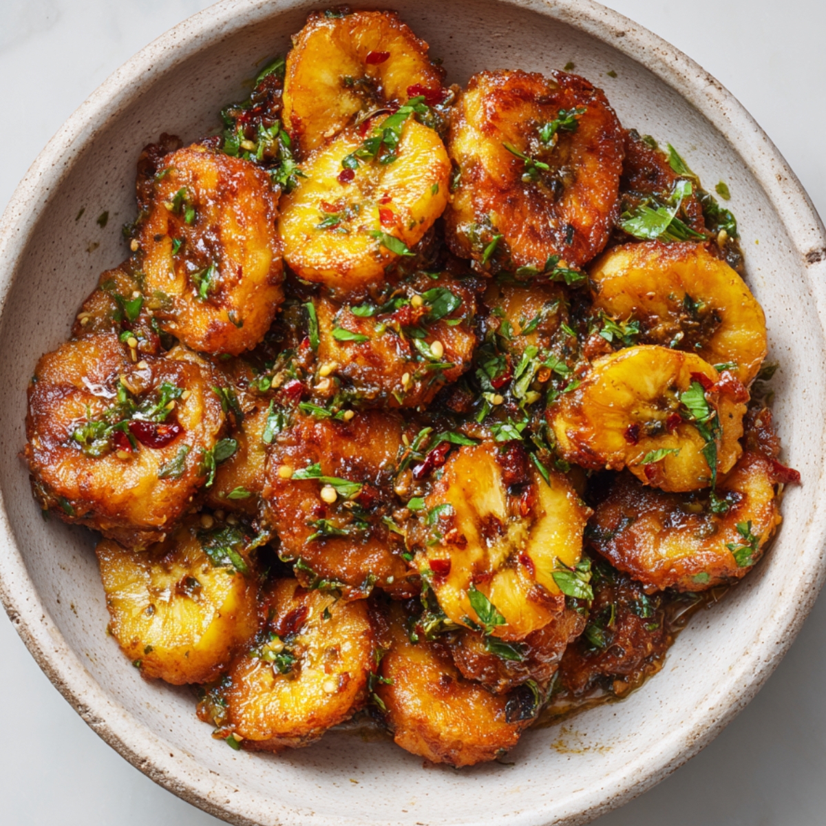 "A bowl of fried plantains with a spicy sauce, garnished with cilantro."