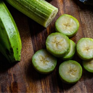 "Fresh green plantains cut into rounds on a wooden cutting board."