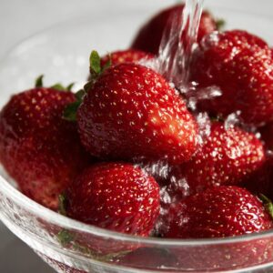 Top view of a blender filled with fresh strawberries, lemon slices, and ice, ready to be blended for juice.