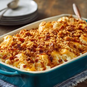 A freshly baked sweet potato casserole in a teal ceramic baking dish. The casserole is topped with a golden-brown, crispy crumble made of brown sugar and bacon bits.