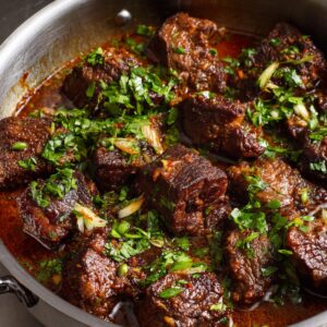 Tender chunks of beef simmering in a flavorful sauce, topped with freshly chopped herbs.