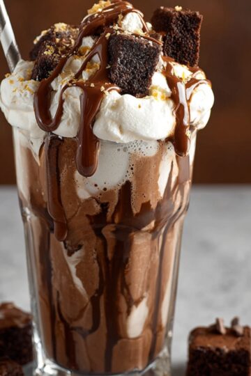 “Decadent brownie milkshake topped with whipped cream, brownie chunks, and chocolate drizzle in a tall glass.”