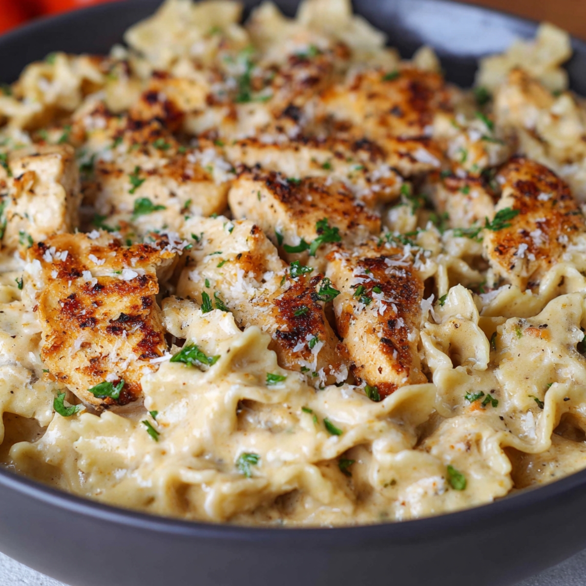 “Bowl of creamy garlic parmesan Chicken pasta with golden seared chicken pieces, garnished with parsley and grated cheese.”