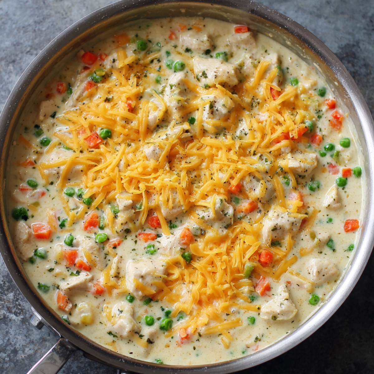 “Creamy chicken pot pie filling in a skillet with diced carrots, peas, and shredded cheddar cheese.”