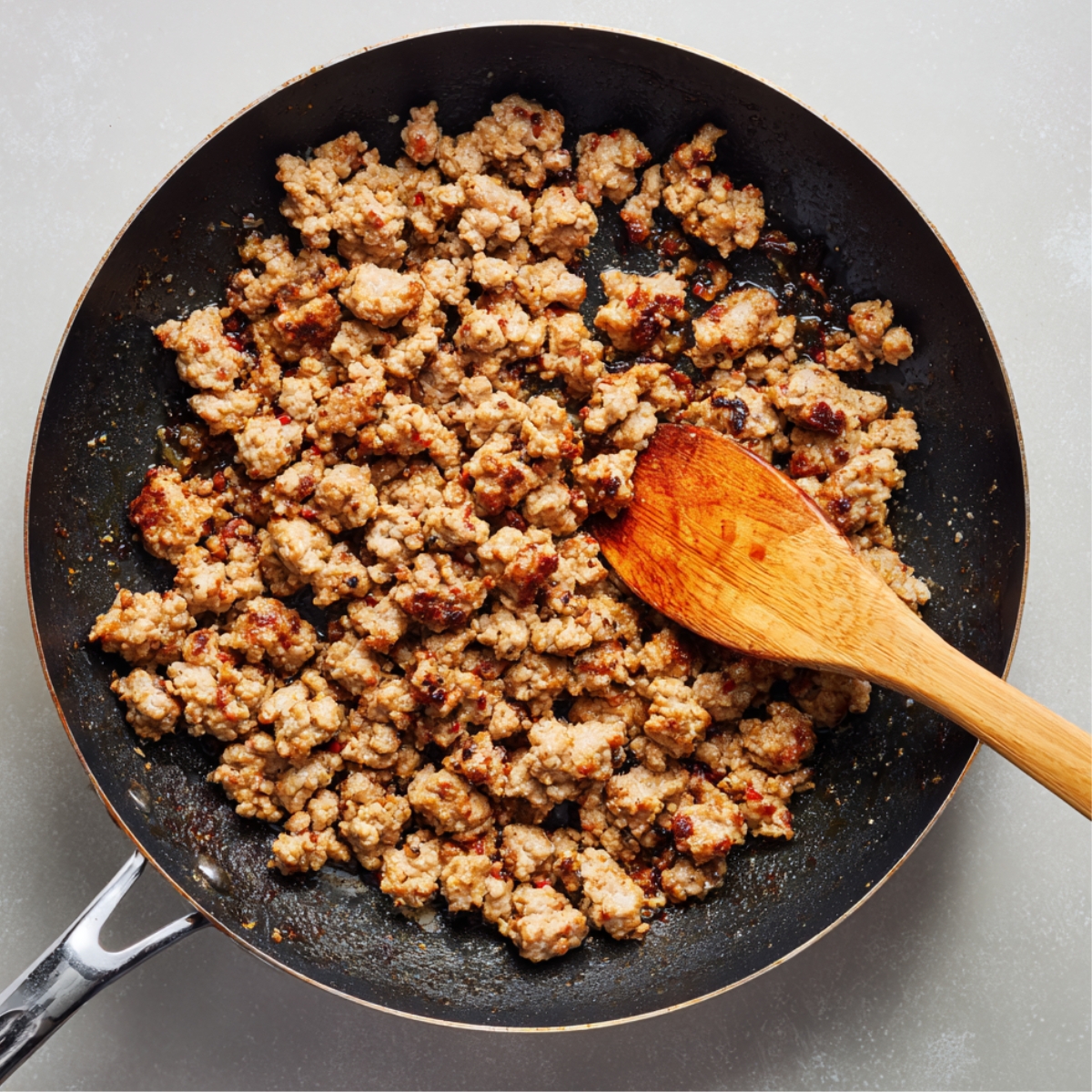 “Crumpled browned sausage cooking in a frying pan with a wooden spatula.”