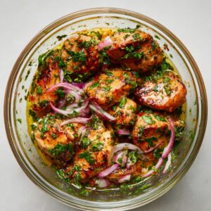 Glazed grilled chicken topped with sliced green onions, served with fresh cucumber and chili garnishes on a ceramic plate.