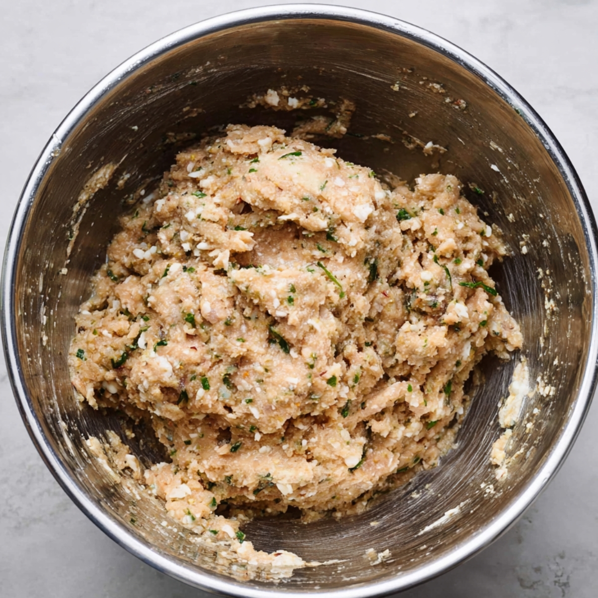 Close-up of mixed garlic parmesan chicken meatloaf mixture in a stainless steel bowl, showing a thick textured blend with herbs and breadcrumbs.”