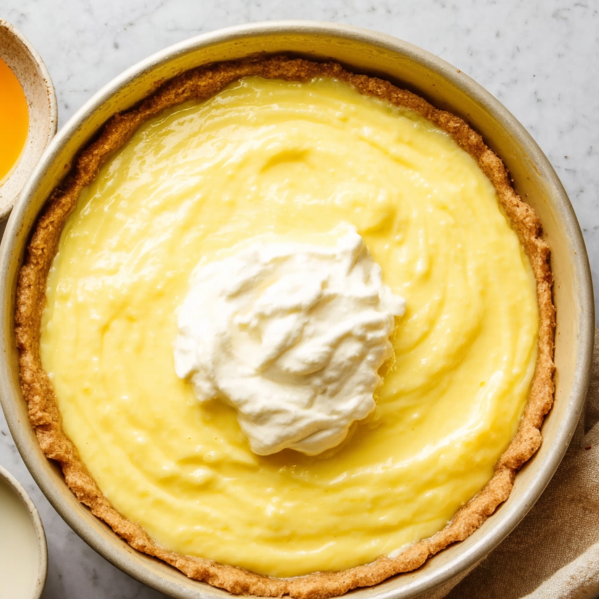 A freshly made lemon cream pie, with a golden, crumbly crust filled with smooth, yellow lemon filling. A generous scoop of whipped cream is placed in the center of the pie, adding a creamy and inviting touch. The pie is perfectly set, ready to be served.