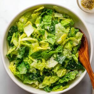 A fresh bowl of chopped romaine lettuce, possibly with some seasoning or dressing on top. There is a wooden spoon beside the salad.