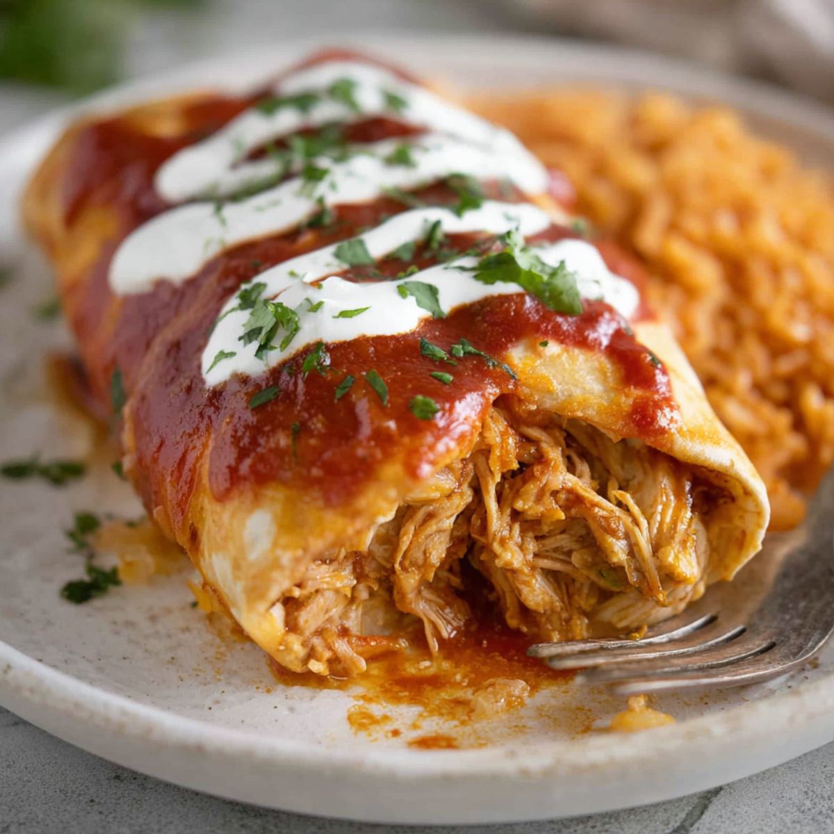 Chicken Chimichangas Close-up of a chicken chimichanga cut open, topped with red sauce, sour cream, and chopped cilantro, served with Mexican rice on a plate.