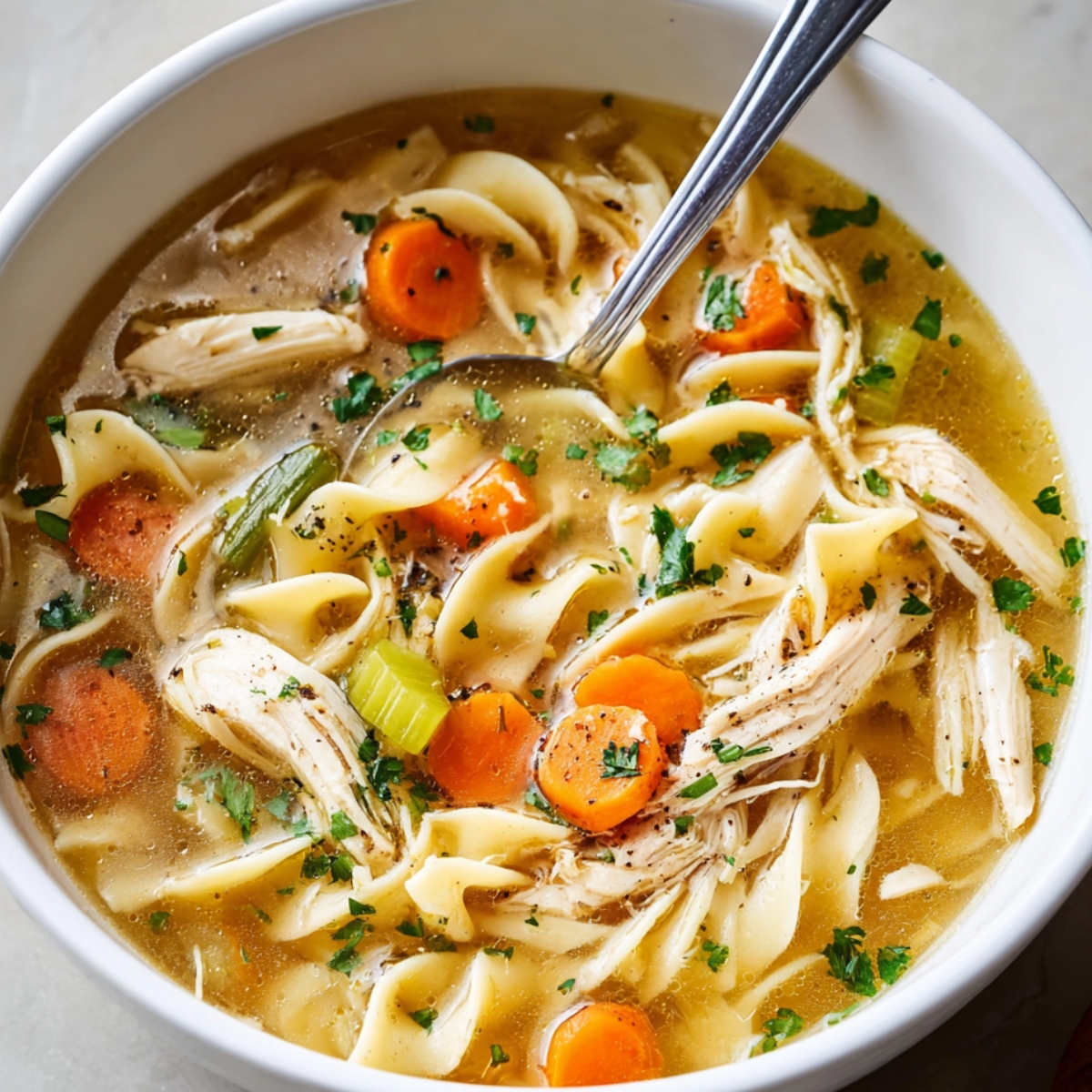 Chicken Noodle Soup A comforting bowl of chicken noodle soup filled with carrots, celery, and tender shredded chicken, garnished with fresh parsley and black pepper."