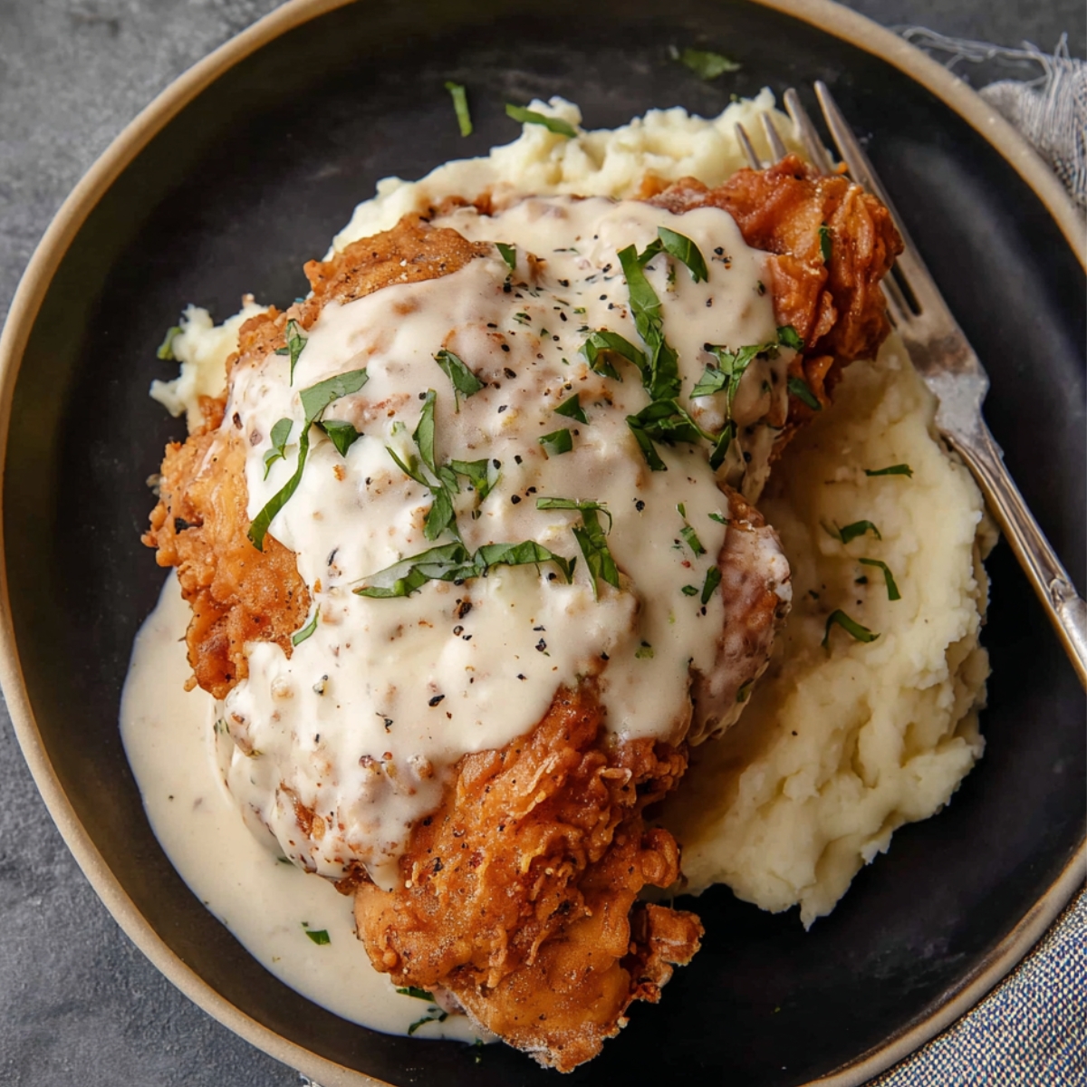 Southern Chicken Fried Chicken with Gravy The final image displays a plate of fried chicken served over mashed potatoes, with a creamy sauce drizzled over the chicken. Fresh herbs are sprinkled on top, providing a well-composed and visually appealing plate of comfort food.