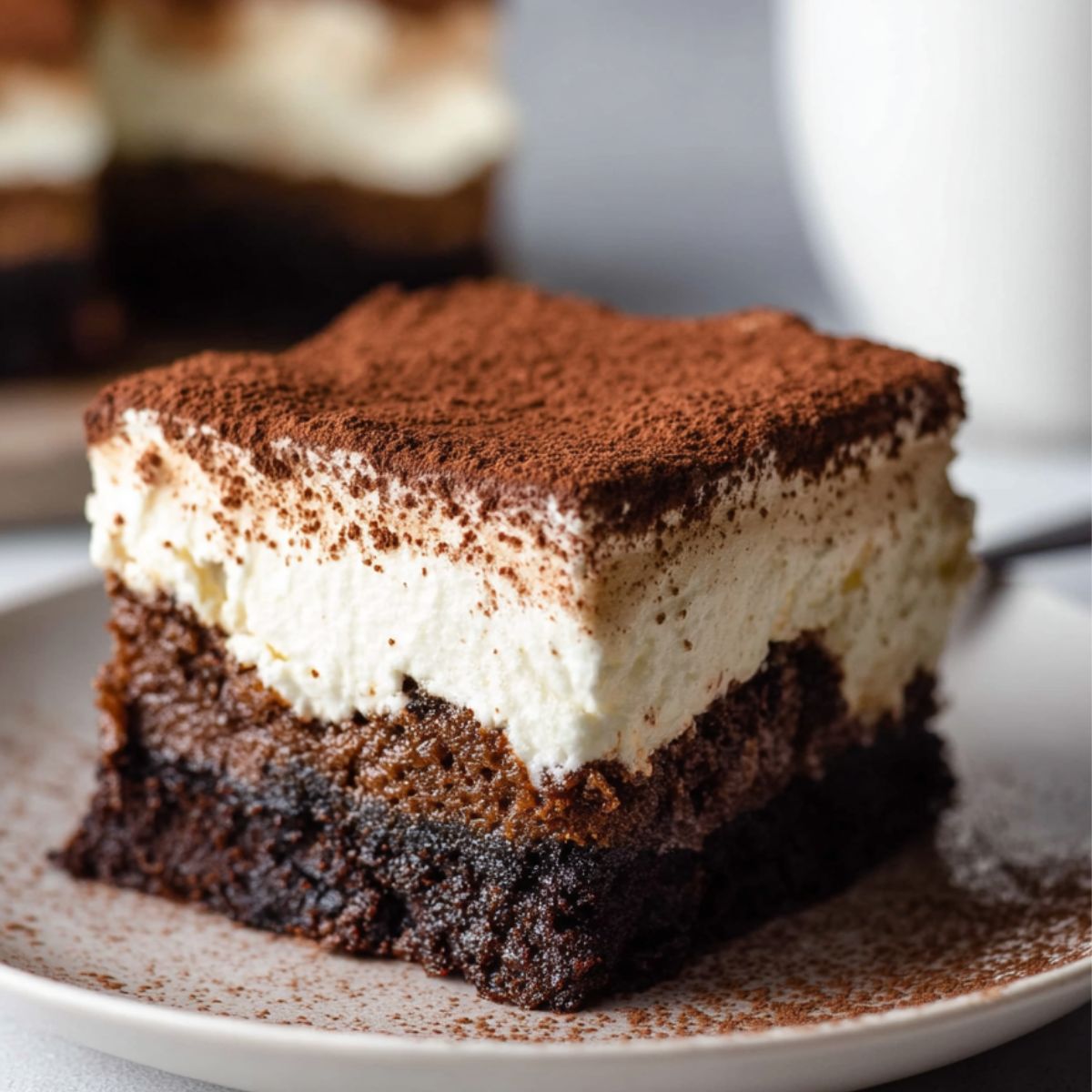 Tiramisu Brownies A close-up of a slice of tiramisu brownies, showing layers of fudgy brownie and creamy mascarpone topped with a dusting of cocoa powder.
