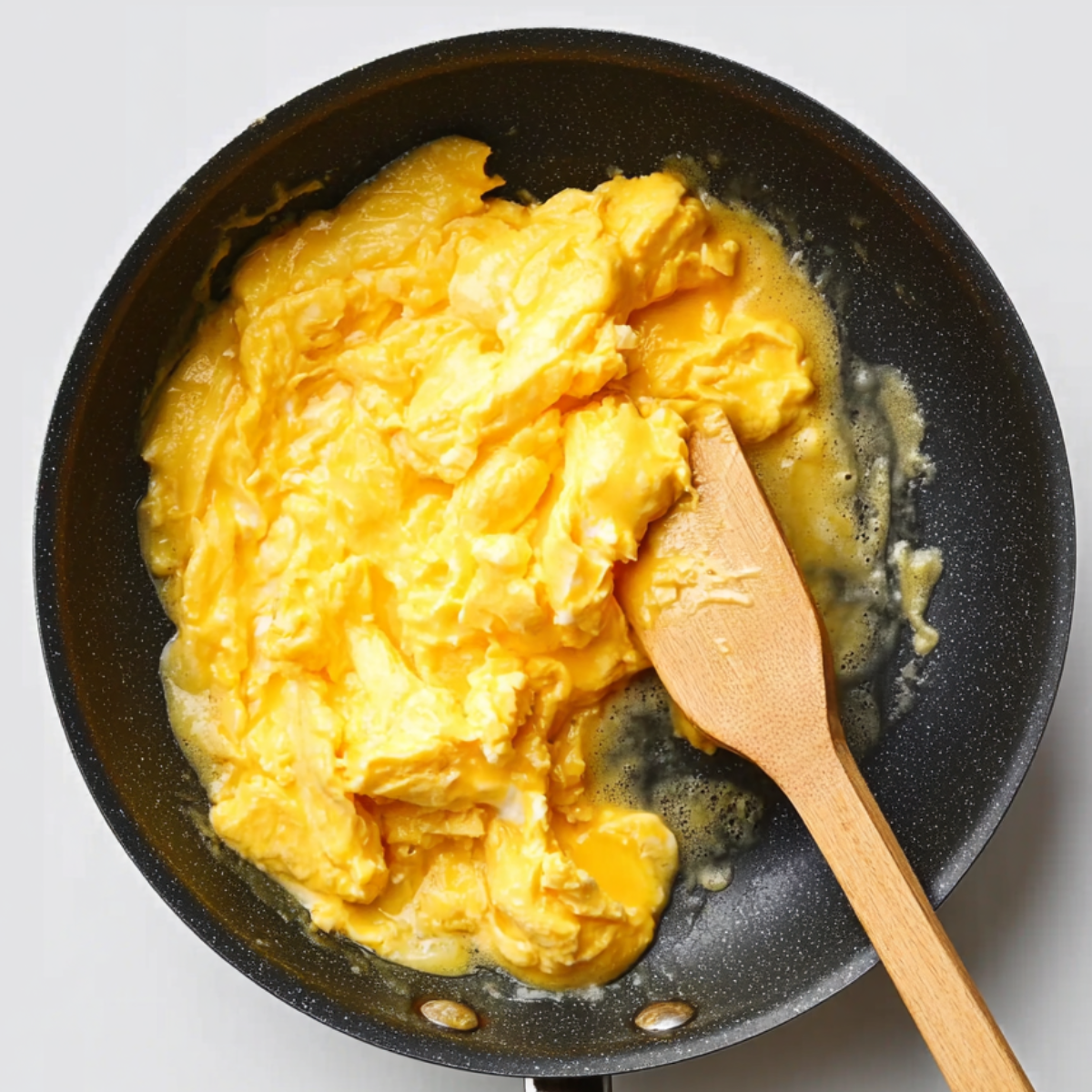 Creamy scrambled eggs cooking in a nonstick skillet, gently folded with a wooden spatula.