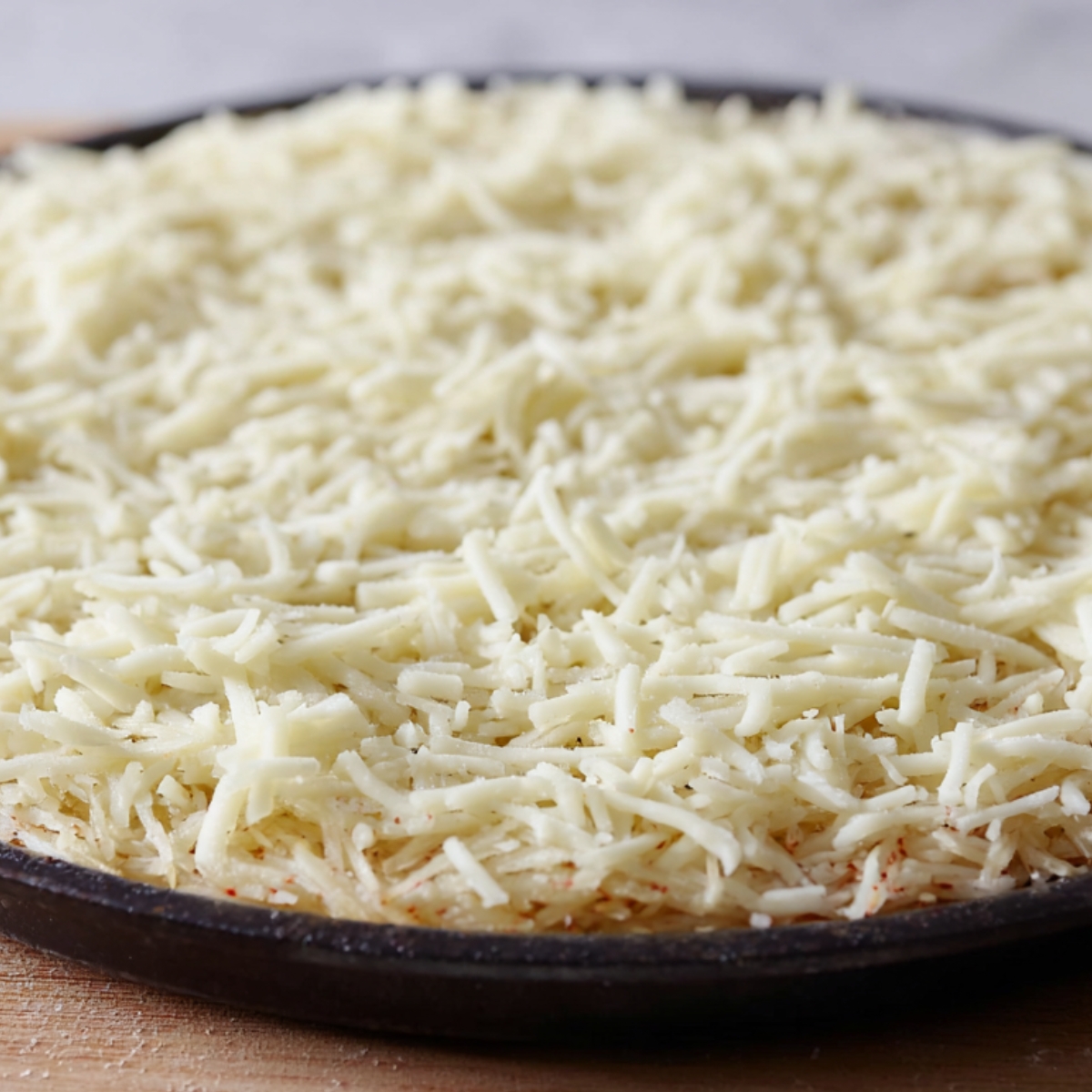 Uncooked breakfast pizza crust made from pressed shredded potatoes spread evenly in a round pan before baking.