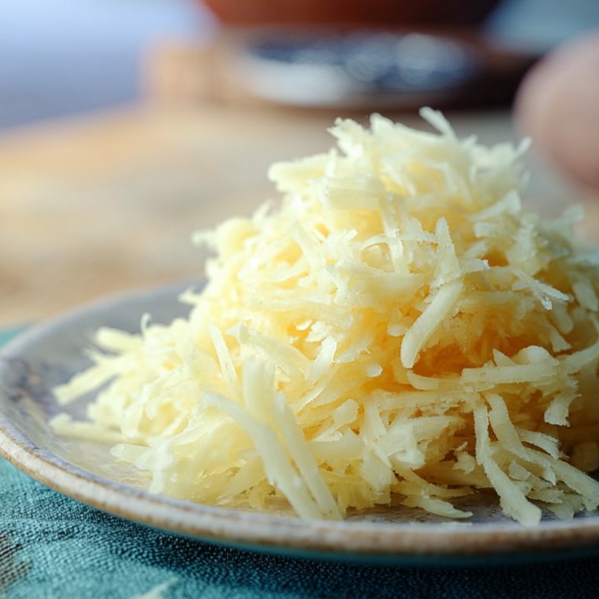 Freshly grated apple piled on a small plate, pale yellow shreds with a moist texture on a rustic surface.
