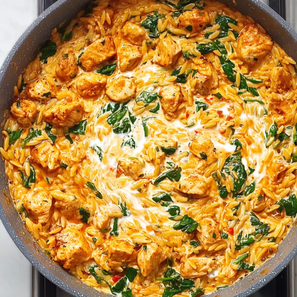 Creamy Cajun chicken orzo cooking in a skillet with spinach, tender chicken chunks, orzo pasta, and swirls of creamy Cajun sauce.