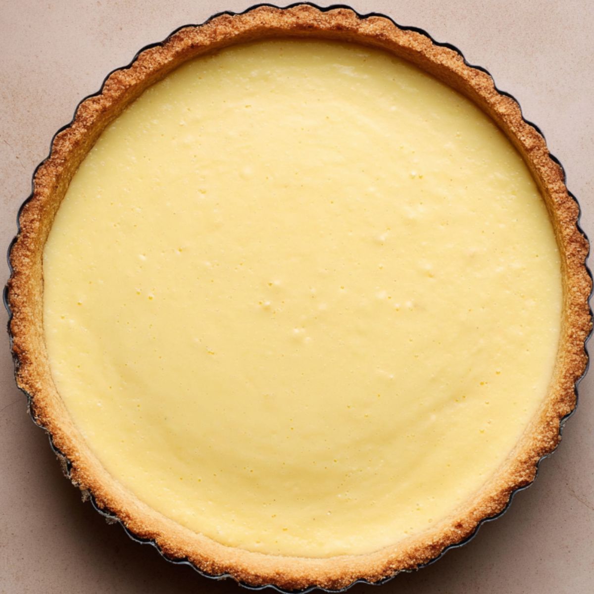 A tart with a buttery, flaky crust filled with creamy vanilla custard, awaiting a topping of fresh fruit. The filling is smooth and golden, with subtle vanilla specks visible.