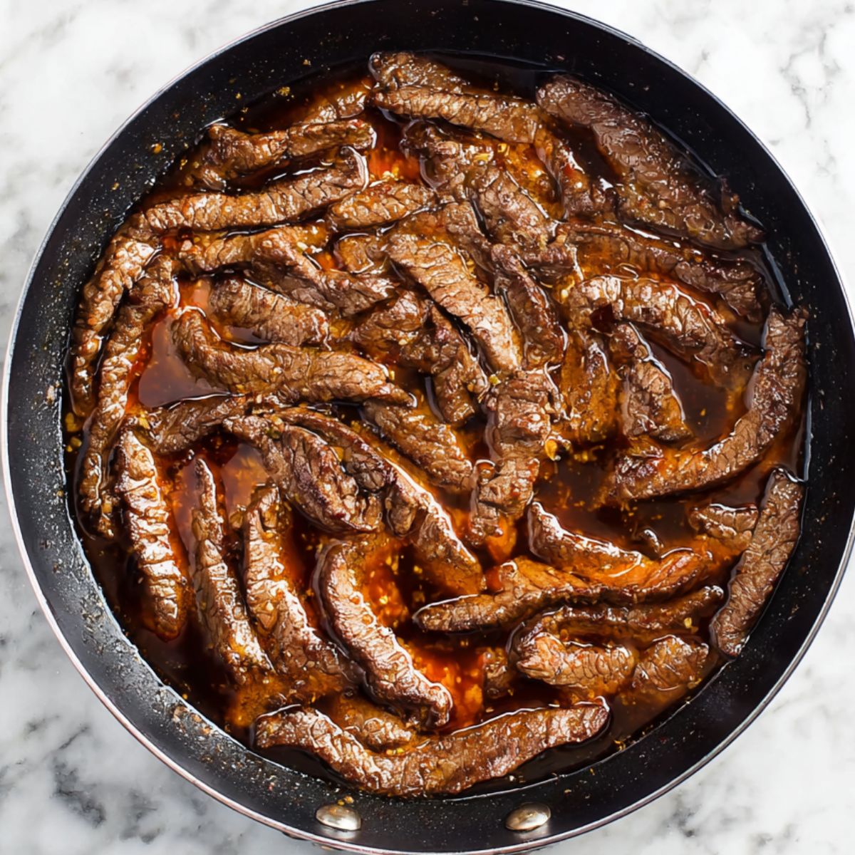Marinated beef strips sizzling in a skillet, cooking in a rich, flavorful sauce. The beef is perfectly tender and soaks up the marinade, creating a deliciously savory aroma. The pan is set on a marble countertop, showcasing the delicious, bubbling beef strips as they cook to perfection.