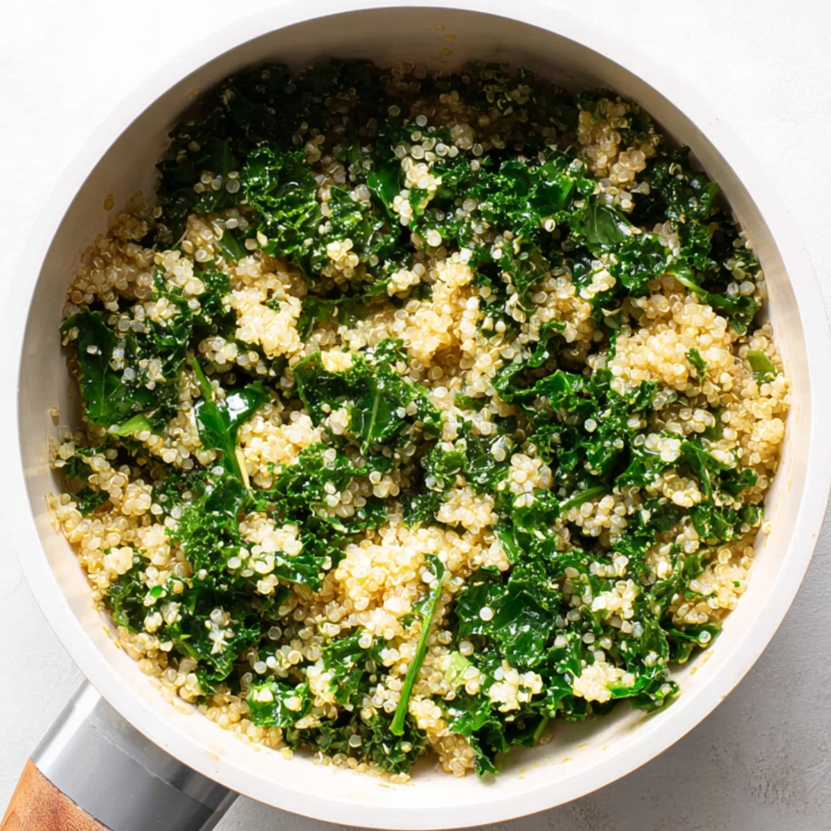 Cooked quinoa mixed with sautéed kale in a white saucepan, lightly coated with olive oil and seasoning.