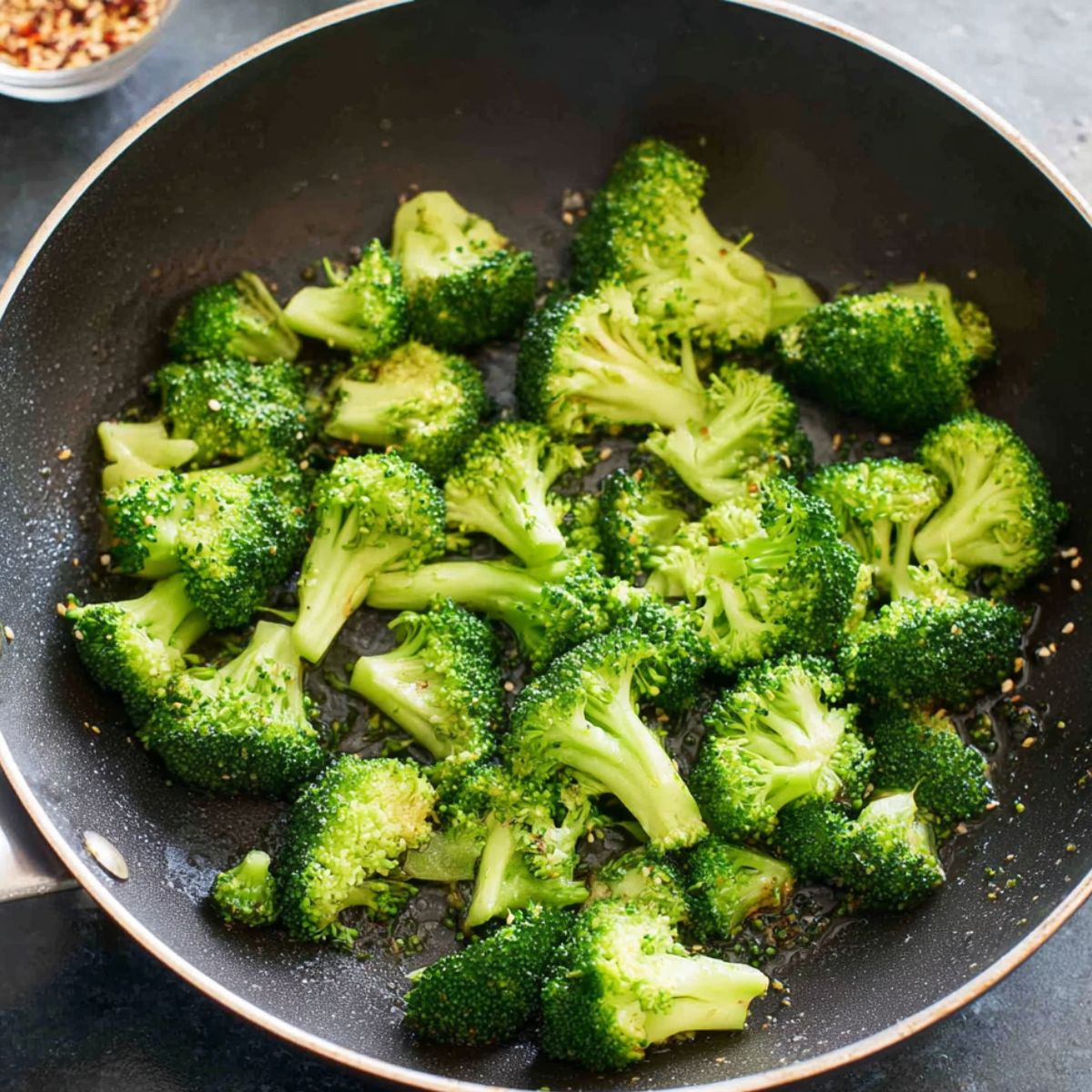 Showcase fresh broccoli florets gently sautéing in a non-stick skillet, their vibrant green color enhanced as they cook. The broccoli is perfectly crisp-tender, lightly seasoned, and ready to complement the other ingredients for a healthy meal.