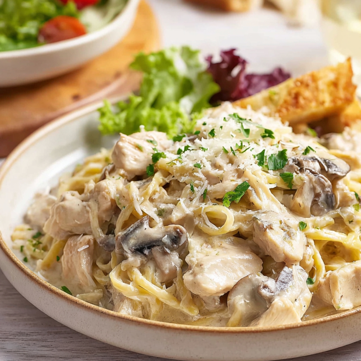 Crockpot Chicken Tetrazzini Creamy Crockpot Chicken Tetrazzini served on a beige plate with tender chicken, mushrooms, pasta in rich white sauce, topped with parsley and parmesan, with salad and garlic bread on the side.