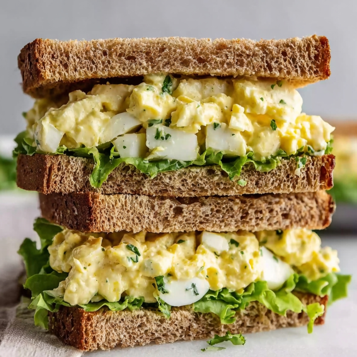 Easy Egg Salad Close-up of a stacked egg salad sandwich on whole wheat bread, layered with creamy egg salad and fresh lettuce, perfect for a satisfying lunch or snack.
