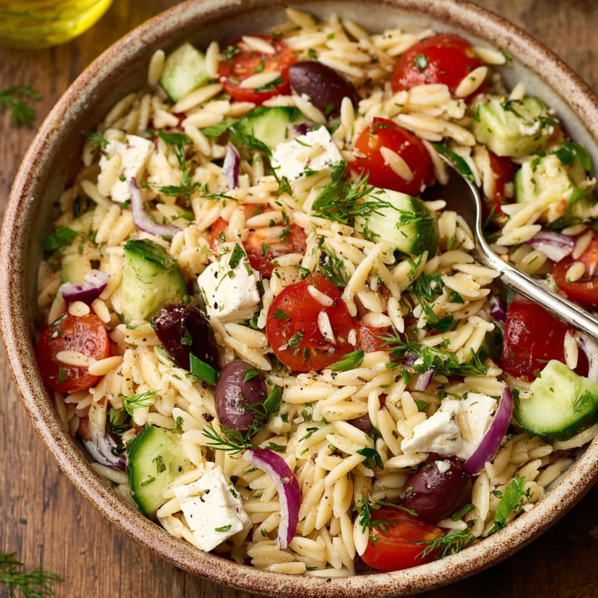 Greek Orzo Salad Close-up of homemade Greek orzo salad in a rustic bowl with cherry tomatoes, cucumber, red onion, Kalamata olives, feta cheese, and fresh herbs.