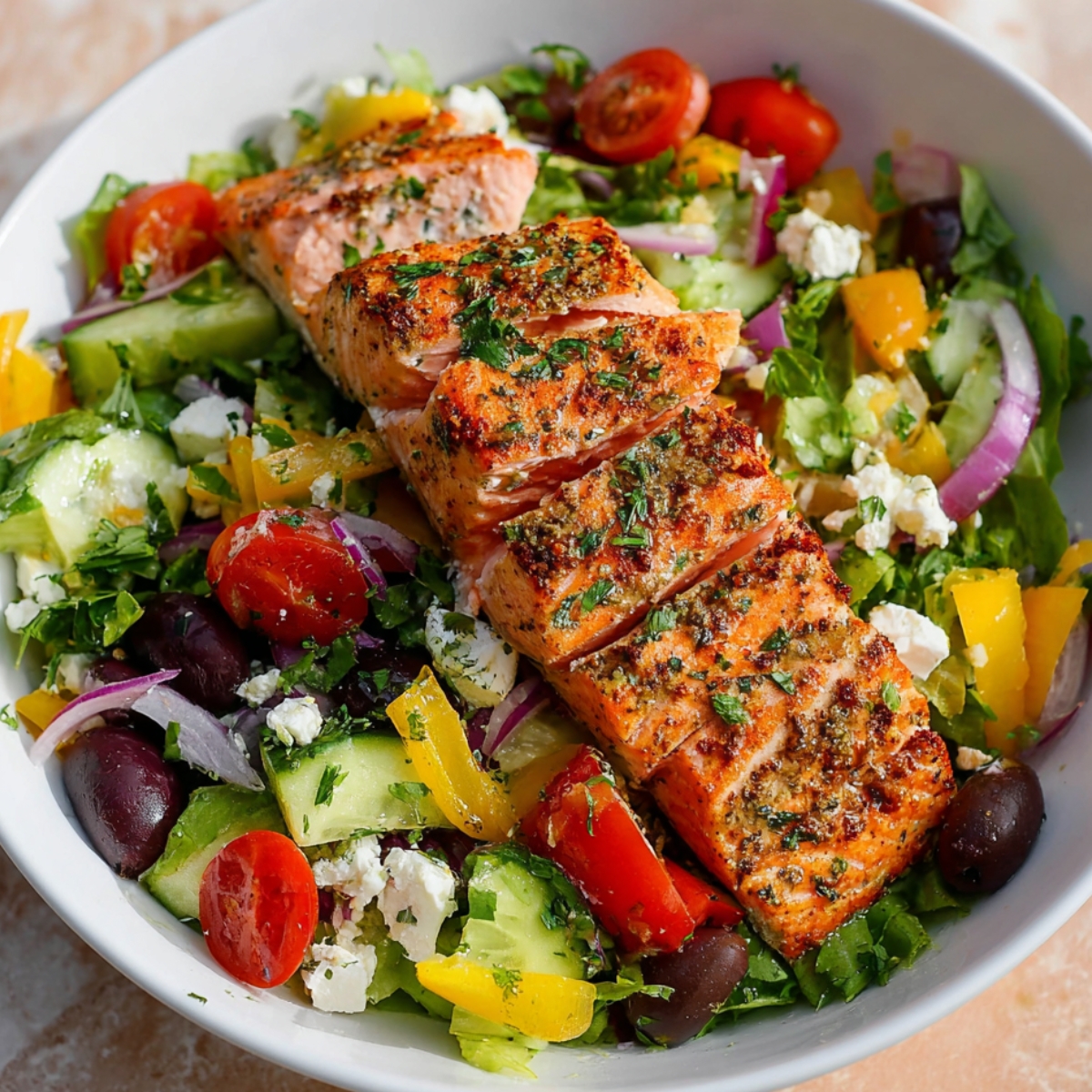 Mediterranean Salmon Salad A bowl filled with fresh Mediterranean salad, topped with perfectly grilled salmon fillets, sliced and seasoned with herbs. The salad includes vibrant ingredients like cherry tomatoes, cucumber, red onions, yellow bell peppers, Kalamata olives, and feta cheese, garnished with fresh herbs like parsley.