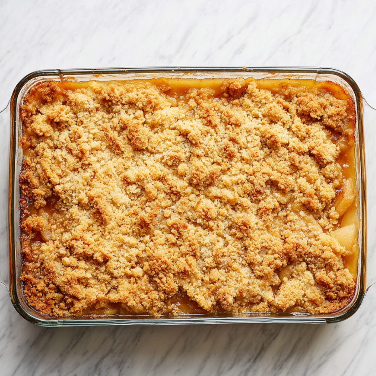 Golden brown apple dump cake baked in a rectangular glass dish with a buttery crumb topping and caramelized edges on a marble surface.