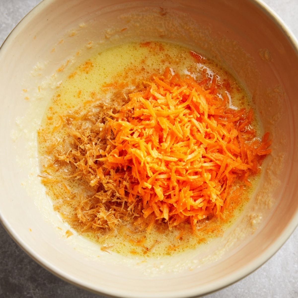Close up of grated carrots added to wet ingredients – Freshly grated carrots mixing into the batter for a flavorful carrot cake or muffin recipe.