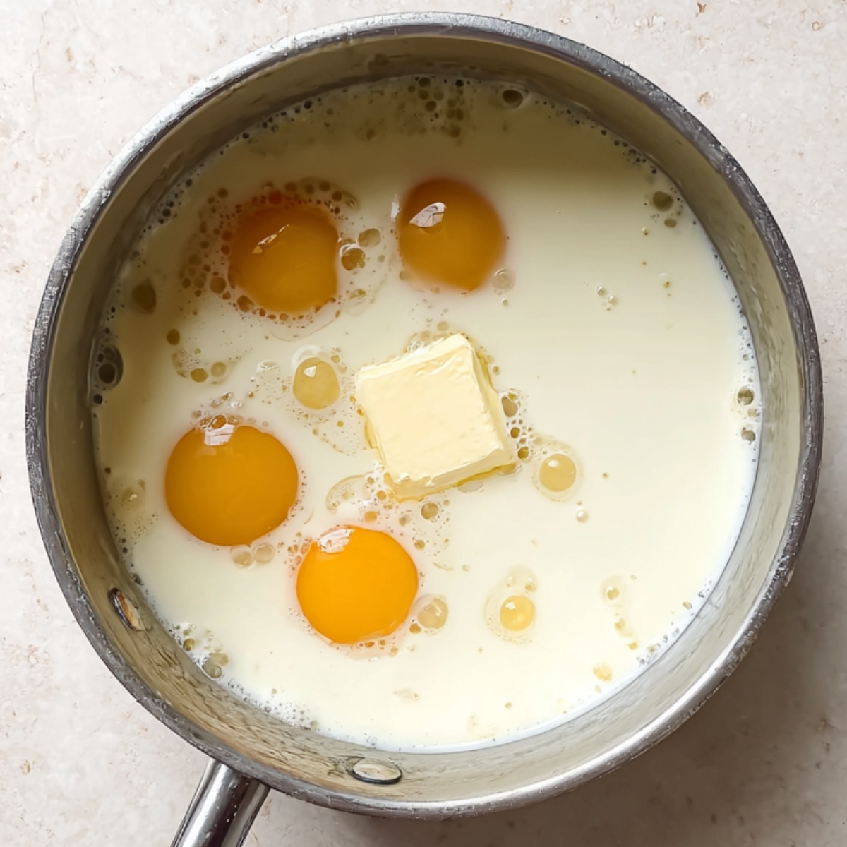 Overhead shot of a saucepan filled with milk, eggs, and butter for custard mixture used to make cinnamon roll bread pudding.