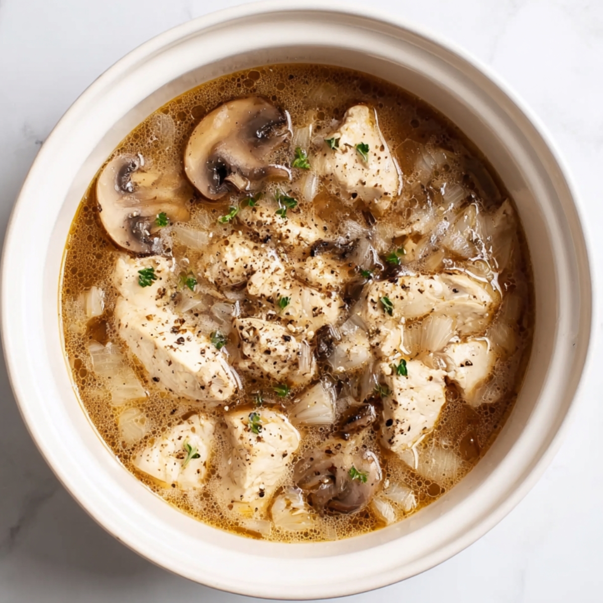 Chicken breasts cooking in crockpot with mushrooms, onions, and seasoned broth for homemade Chicken Tetrazzini.
