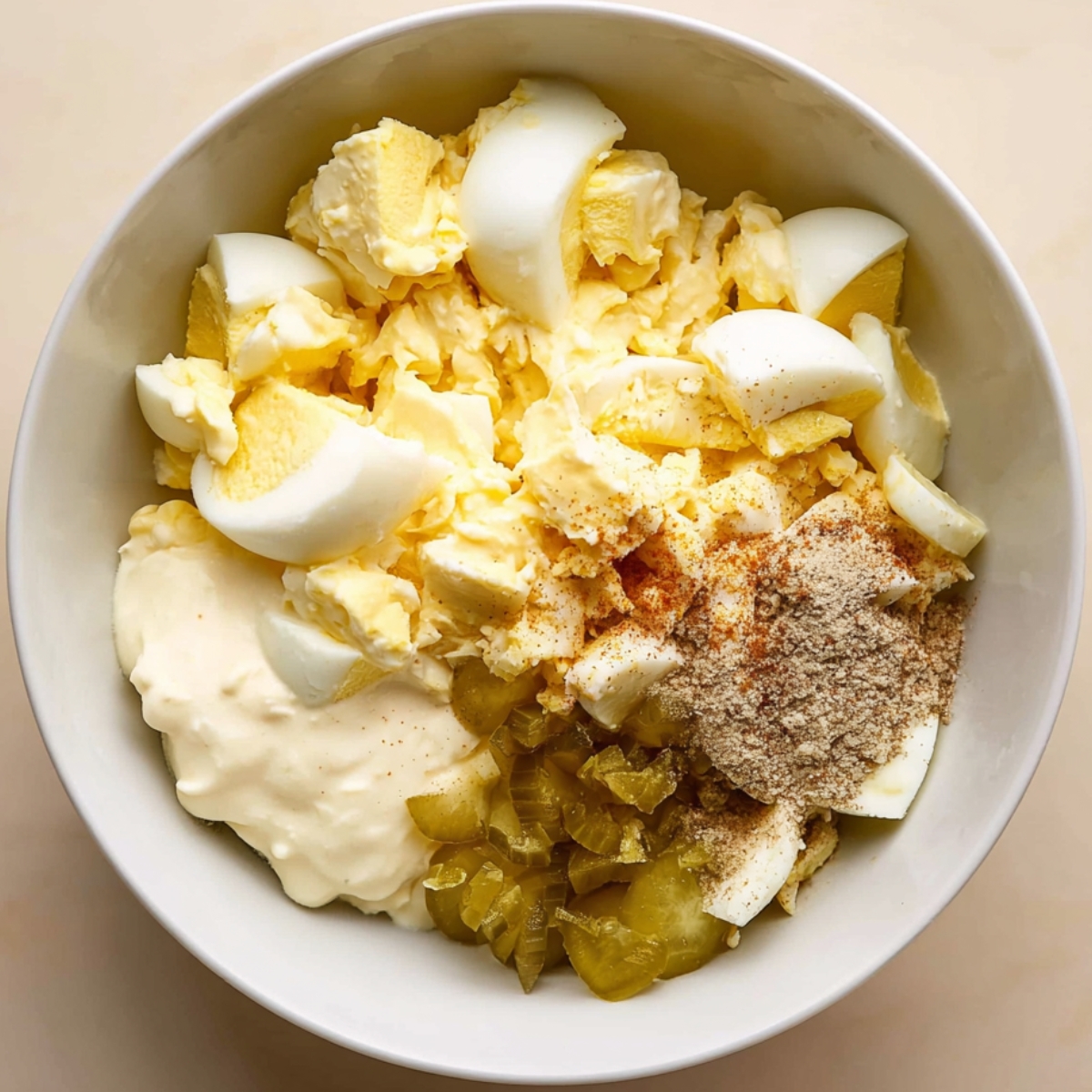 Close-up of a bowl filled with egg salad ingredients: chopped hard-boiled eggs, mayonnaise, pickles, and spices, ready to be mixed into a delicious egg salad.