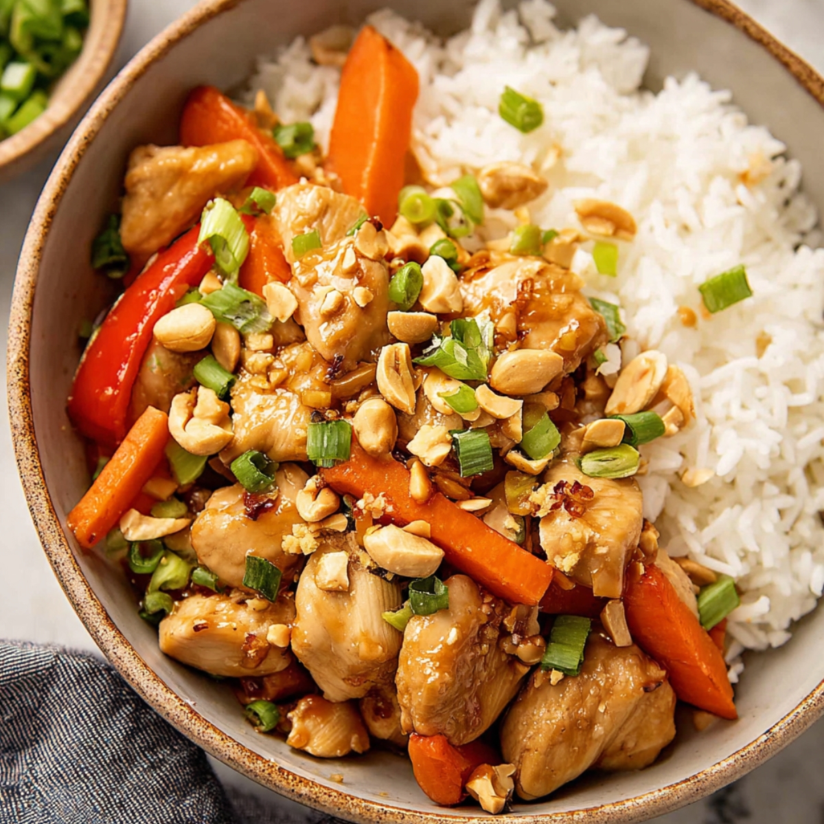 Kung Pao Chicken Close up of a delicious Kung Pao chicken bowl, served on a bed of fluffy rice, topped with vibrant vegetables, peanuts, and fresh green onions.