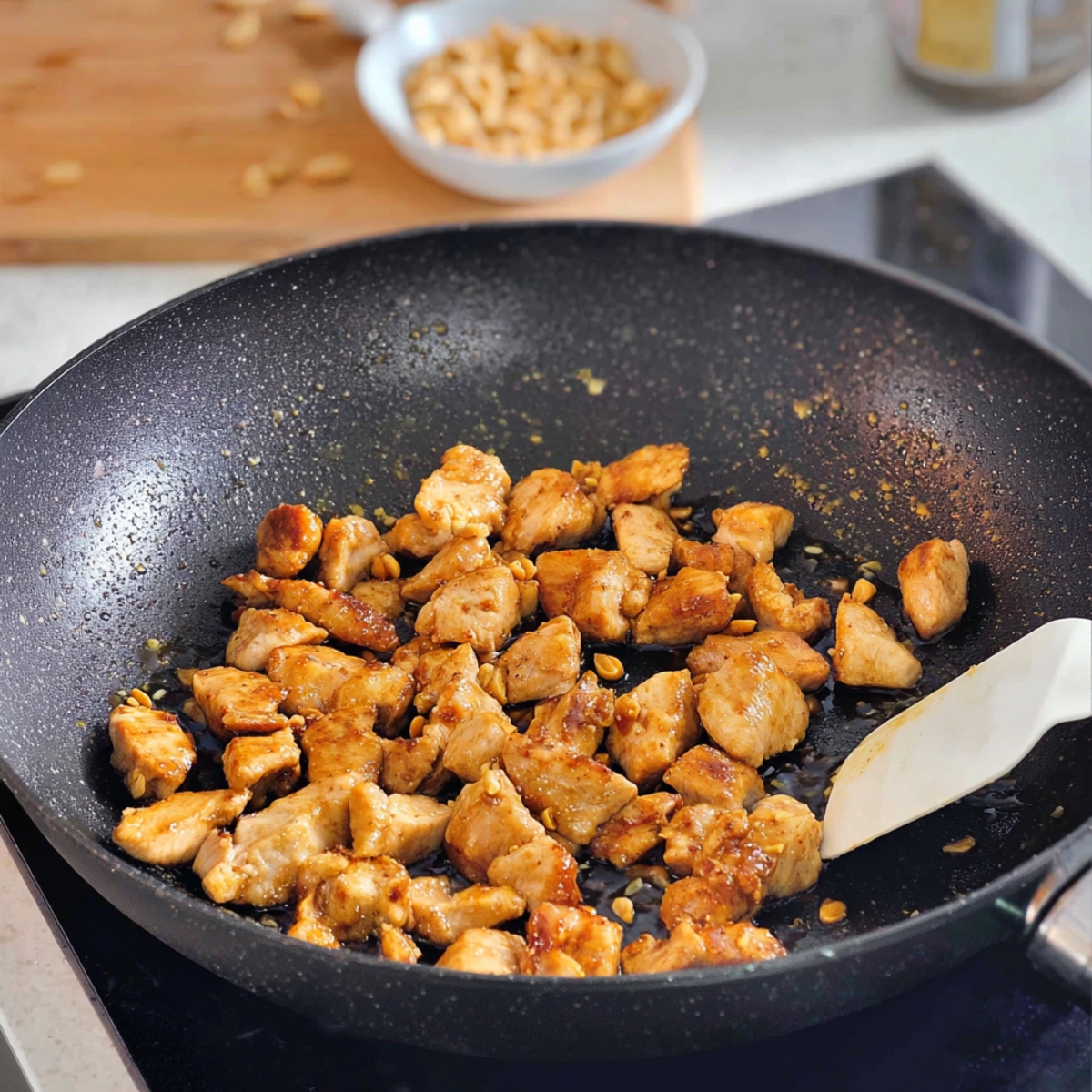 The chicken pieces for the Kung Pao dish are being sautéed in a hot pan with peanuts. The chicken is golden brown, infused with a rich sauce, and ready to be combined with other ingredients for the final dish.
