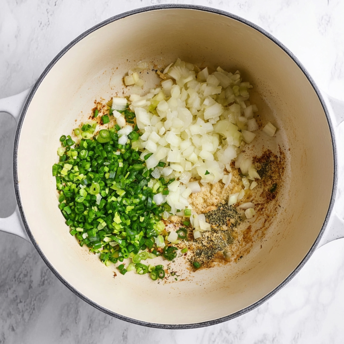 Diced white onions, minced garlic, and chopped jalapeños added to a Dutch oven with browned bits on the bottom during the Texas chili cooking process.