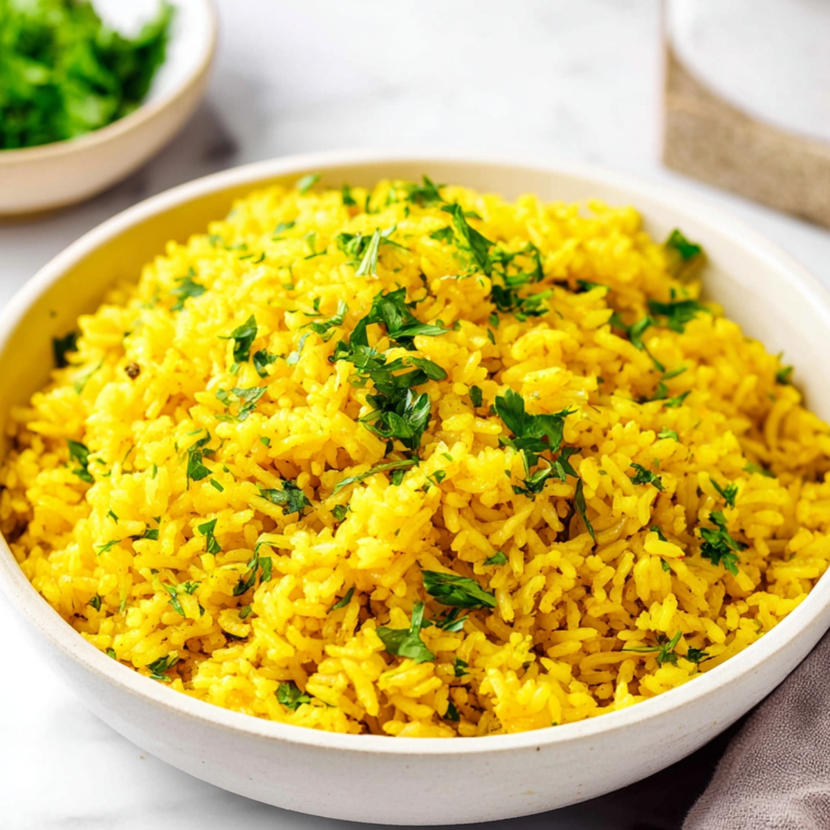 Yellow rice recipe Close-up of fluffy yellow turmeric rice garnished with fresh chopped parsley in a white ceramic bowl on a light kitchen surface with soft natural lighting.