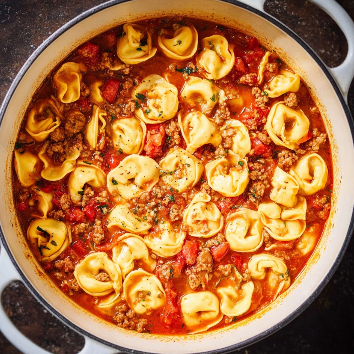 Close up of tortellini pasta simmering in a rich tomato and ground meat sauce in a white cast iron pot, top-down view, vibrant colors, natural lighting, food photography style, high detail