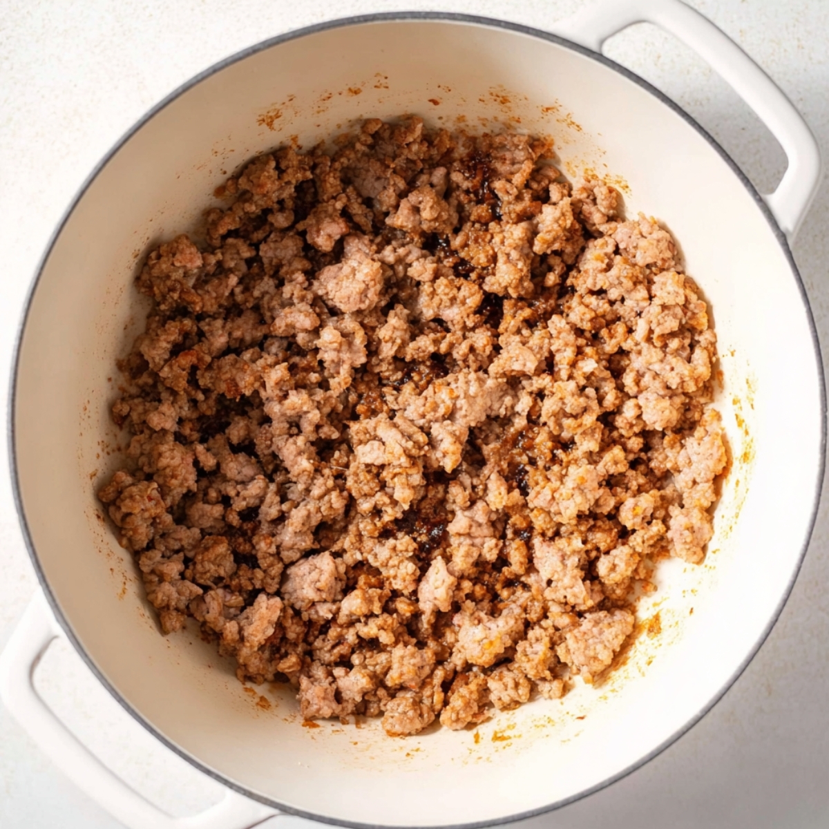 Close up of browned ground meat in a white enameled cast iron pot, showing texture and juicy crumbles, top-down view, natural lighting, food photography style, high detail