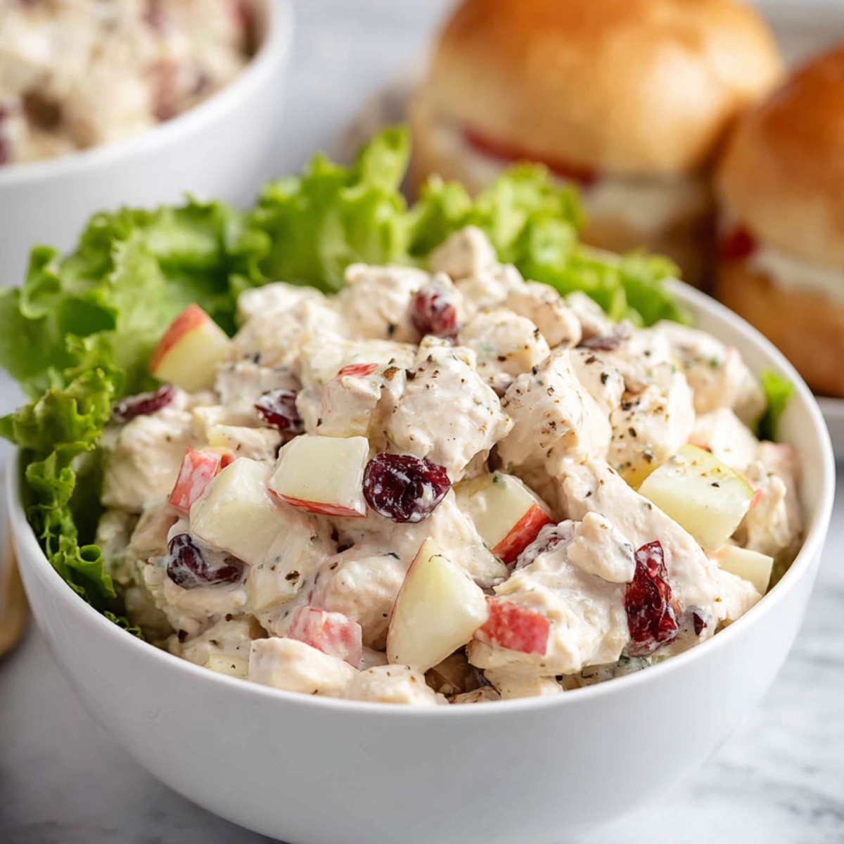 Chicken Salad with Apples Close up of a hearty chicken salad with apples, cranberries, and chicken, served with fresh lettuce and sandwich rolls for a satisfying meal.